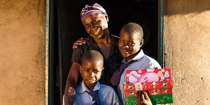 Family holding shoebox gifts in doorway of home