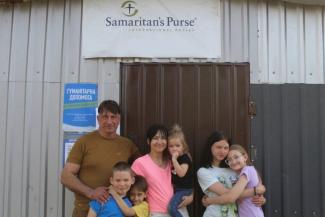 Sergey, his wife, and five of their seven children stand in front of their bakery in their current city.