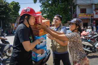 Thuyet, left, stacks food and water she received at a Samaritan’s Purse distribution onto her motorcycle to bring back home to her family.